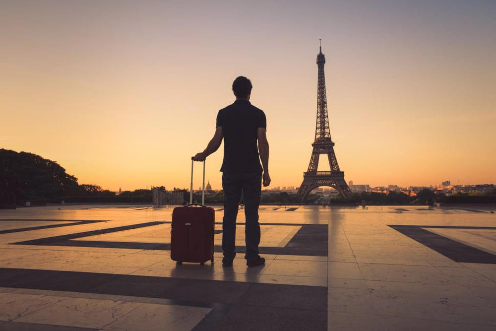 A Nigerian tourist gazes at the Eiffel Tower, clutching a guidebook under a Parisian sunset