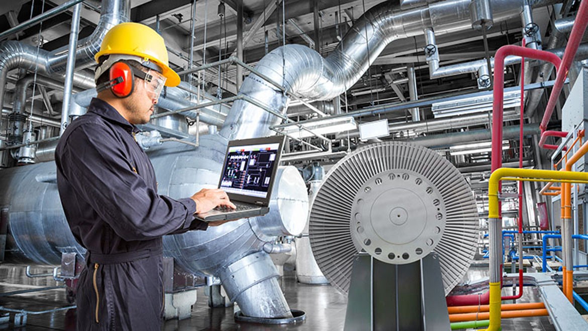 A mechanical engineer from an international background, wearing safety gear, inspects machinery in a modern German factory