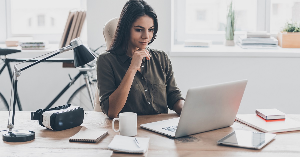 A young professional from an international background, sitting at a desk with a laptop, reviewing documents 